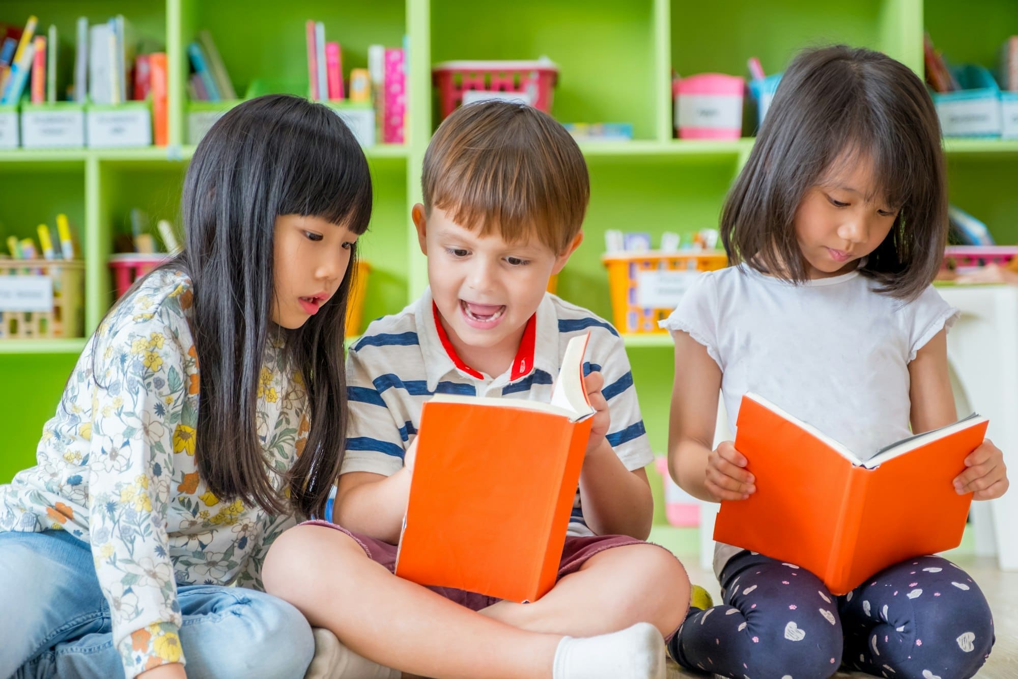 Children sitting on floor and reading tale book in preschool library