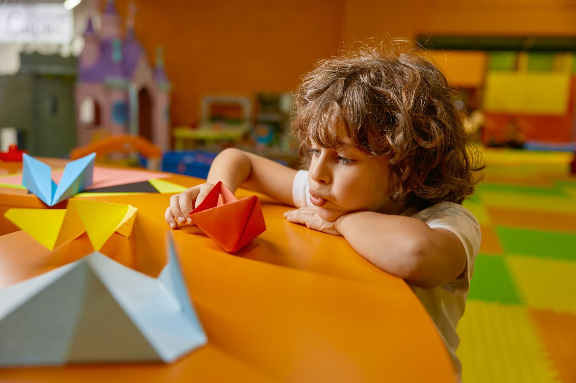 Cute boy child playing handmade origami paper boat at childcare center